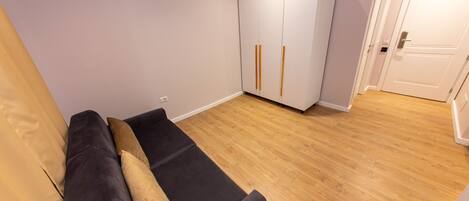 A room with a dark-colored sofa, a white wardrobe with vertical handles, and a wooden floor.