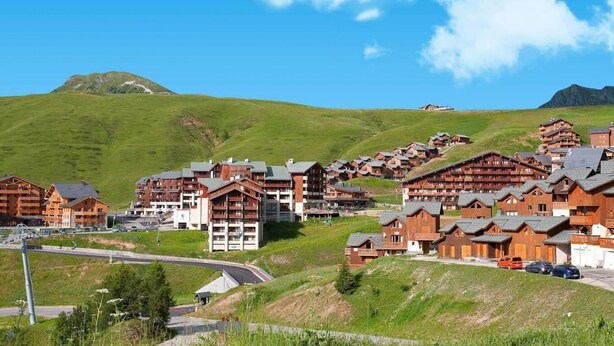A mountain resort with wooden buildings, a winding road, and a clear blue sky.