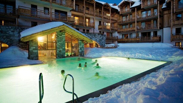 A heated outdoor swimming pool surrounded by snow, with wooden buildings in the background. - Wifi, ski-in/ski-out & foot of the slopes, swimming pool, sauna, hammam, terrace, balcony, tv (Montgenèvre)