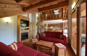 A spacious living area with a red sofa, wooden coffee table, and a fireplace. A kitchen with wooden cabinets and a dining area is visible in the background. - 300m from shops, swimming pool, sauna, hammam, terrace, balcony, tv, ski locker, 31m², Montgenèvre (Montgenèvre)
