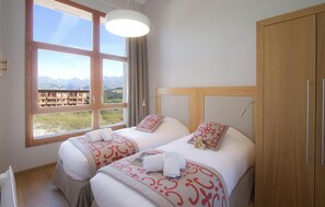 A hotel room with two beds, a large window with a mountain view, a wooden wardrobe, and a hanging light fixture. - Fitness, swimming pool, sauna, hammam, fireplace or stove, tv, ski locker, 76-84m², Les Arcs (Les Arcs)