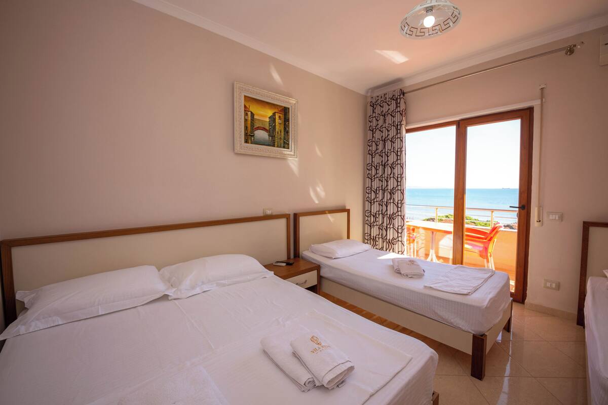 A hotel room with two beds, a painting on the wall, and a balcony with a view.