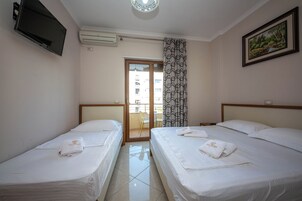 Camera d'albergo con due letti, televisore, condizionatore d'aria, un quadro e vista sul balcone esterno.