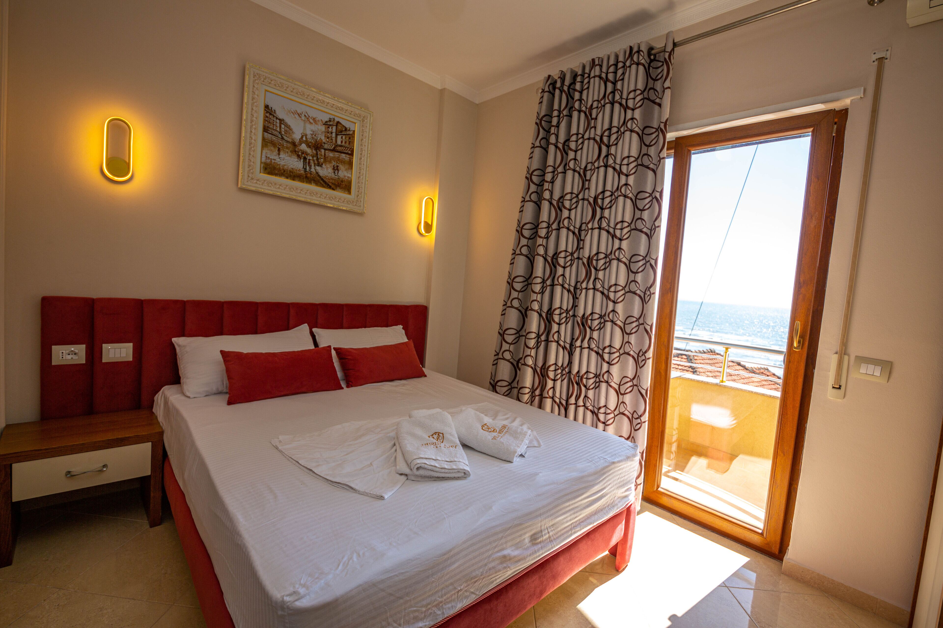 A hotel room with a bed, a nightstand, a window with a view, and a painting on the wall.