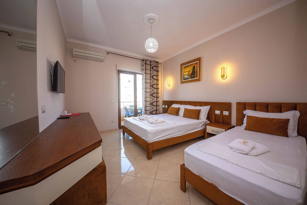 A hotel room with two beds, a wooden desk, a TV, and a painting on the wall.