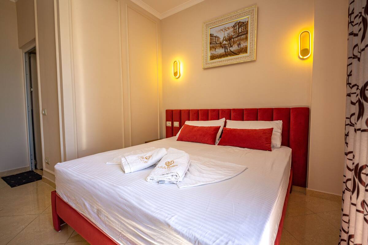 A hotel room with a neatly made bed, a red headboard, and a framed picture on the wall.