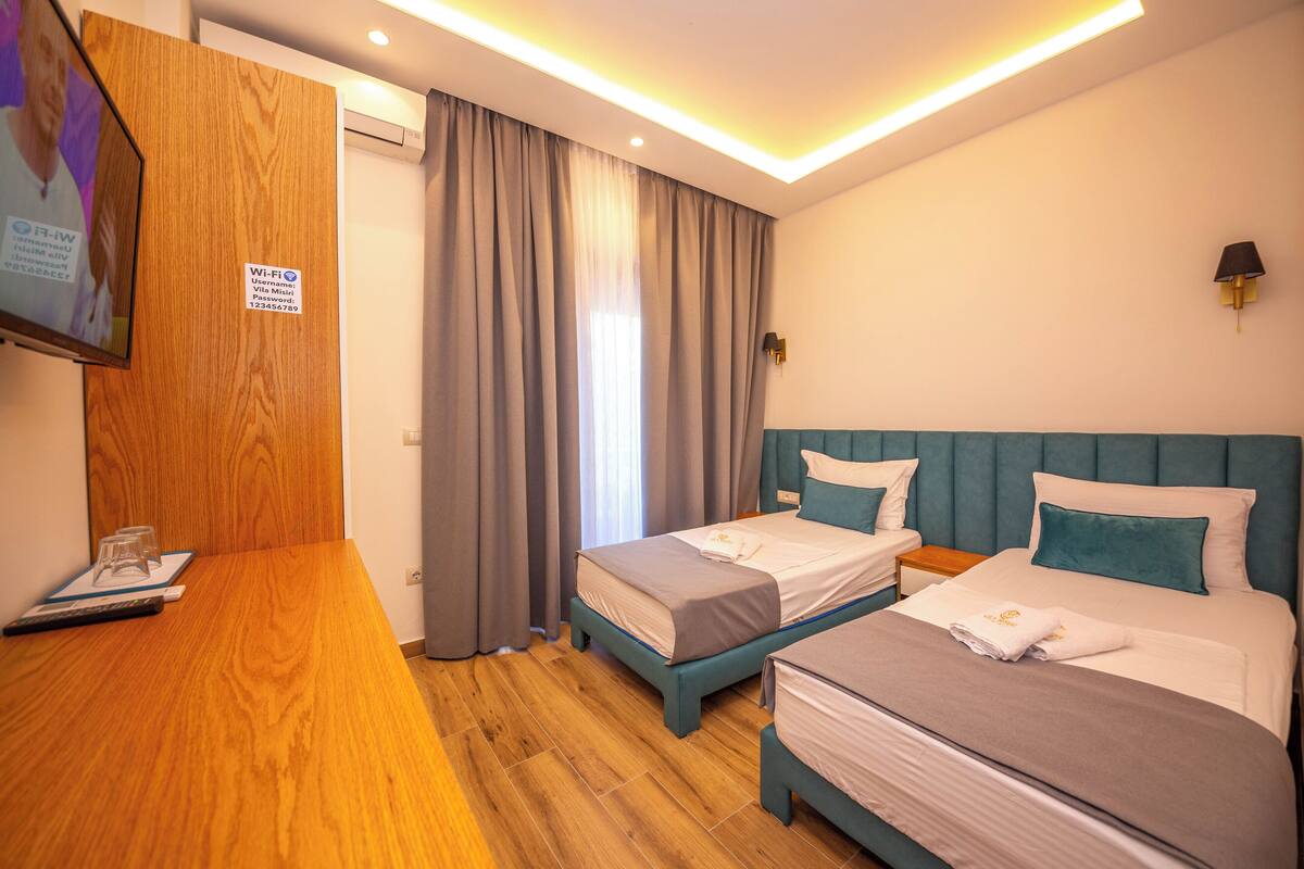 A hotel room with two beds, a wooden desk, a TV, and a sign indicating Wi-Fi availability.