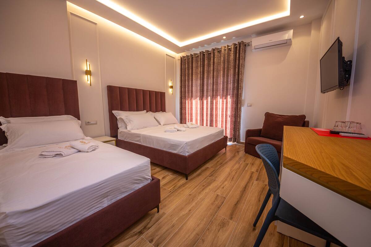 A hotel room with two beds, a desk, a chair, a TV, and a window with curtains.