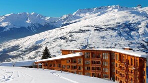 A wooden lodge with multiple balconies, set against a backdrop of snow-covered mountains.