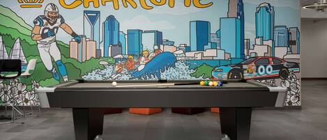 Une table de billard ornée d’une fresque représentant le paysage urbain de Charlotte et des figures sportives.