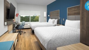 Une chambre d’hôtel avec deux lits, un bureau, une chaise, une télévision et une fenêtre donnant sur des arbres.