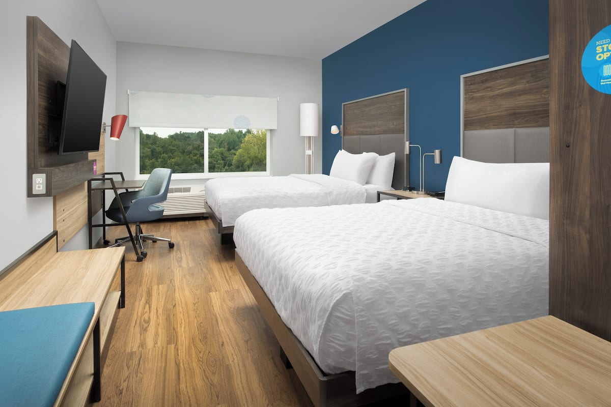Une chambre d’hôtel avec deux lits, un bureau, une chaise, une télévision et une fenêtre donnant sur des arbres.
