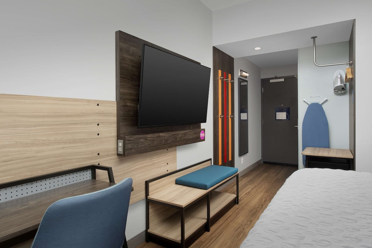 Une chambre d’hôtel moderne équipée d’un lit, d’un bureau avec une chaise, d’un téléviseur fixé au mur et d’un espace douche.
