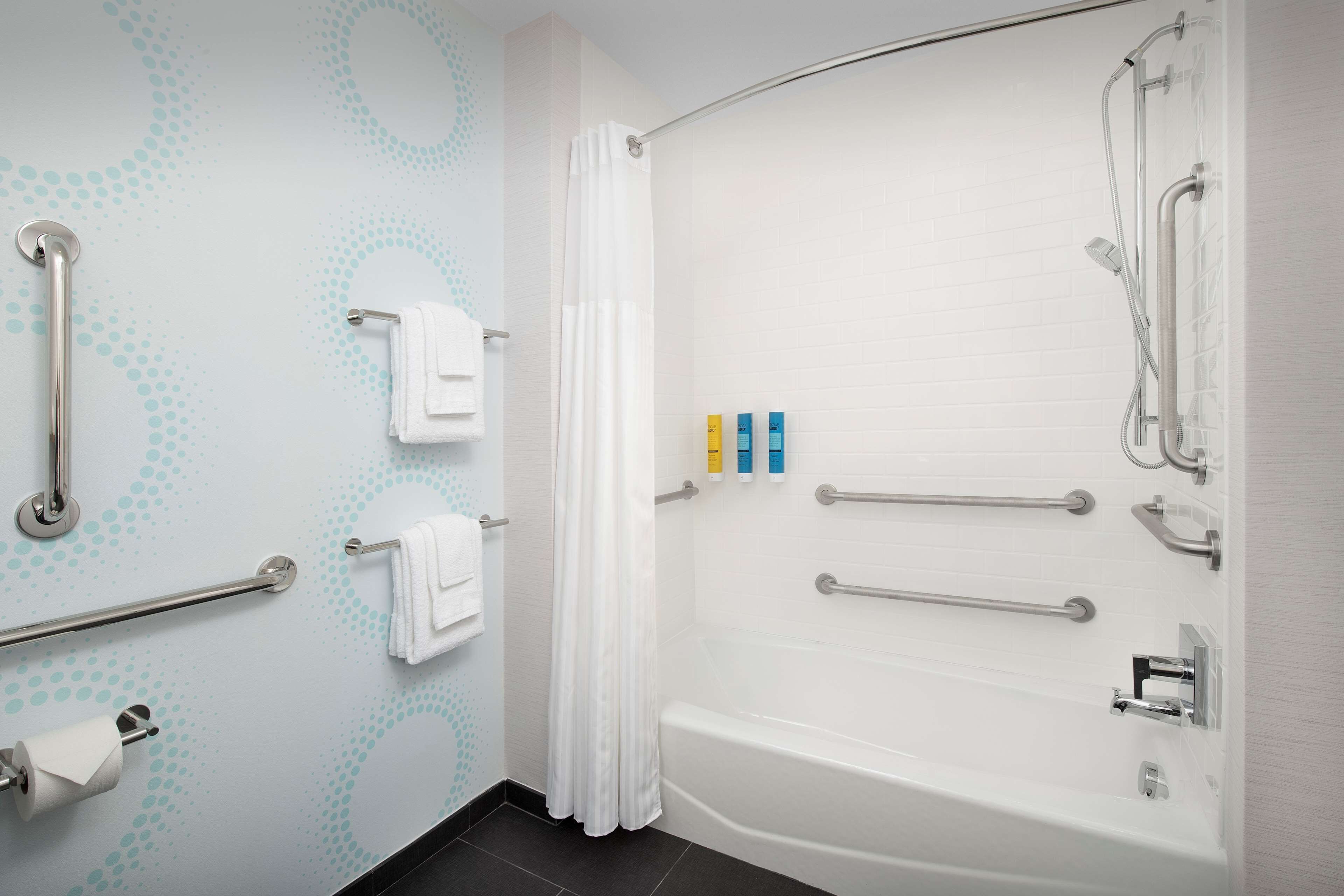 Et moderne badeværelse med badekar, gelænder, bruser med håndbruser og toiletpapirsholder.