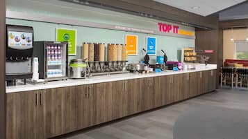A breakfast counter with a coffee machine, a refrigerated display, and various food containers.