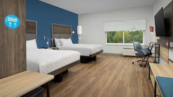 A hotel room with two beds, a desk, a chair, a TV, and a window with a view of trees.