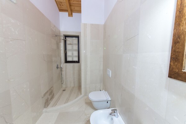 A bathroom with a shower, toilet, and sink, featuring marble tiles and wooden ceiling beams. - Hotel Onufri (Berat)