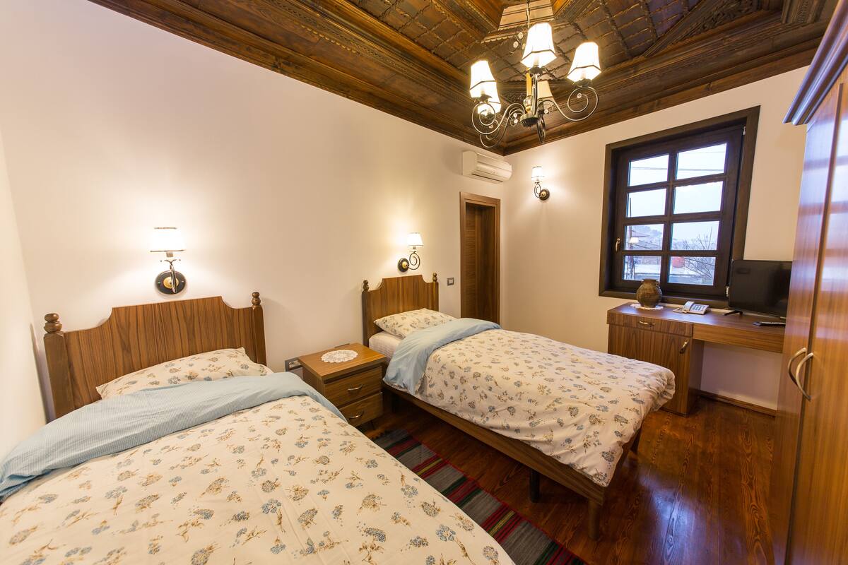 A bedroom with two beds, wooden headboards, a desk with a television, and a window.