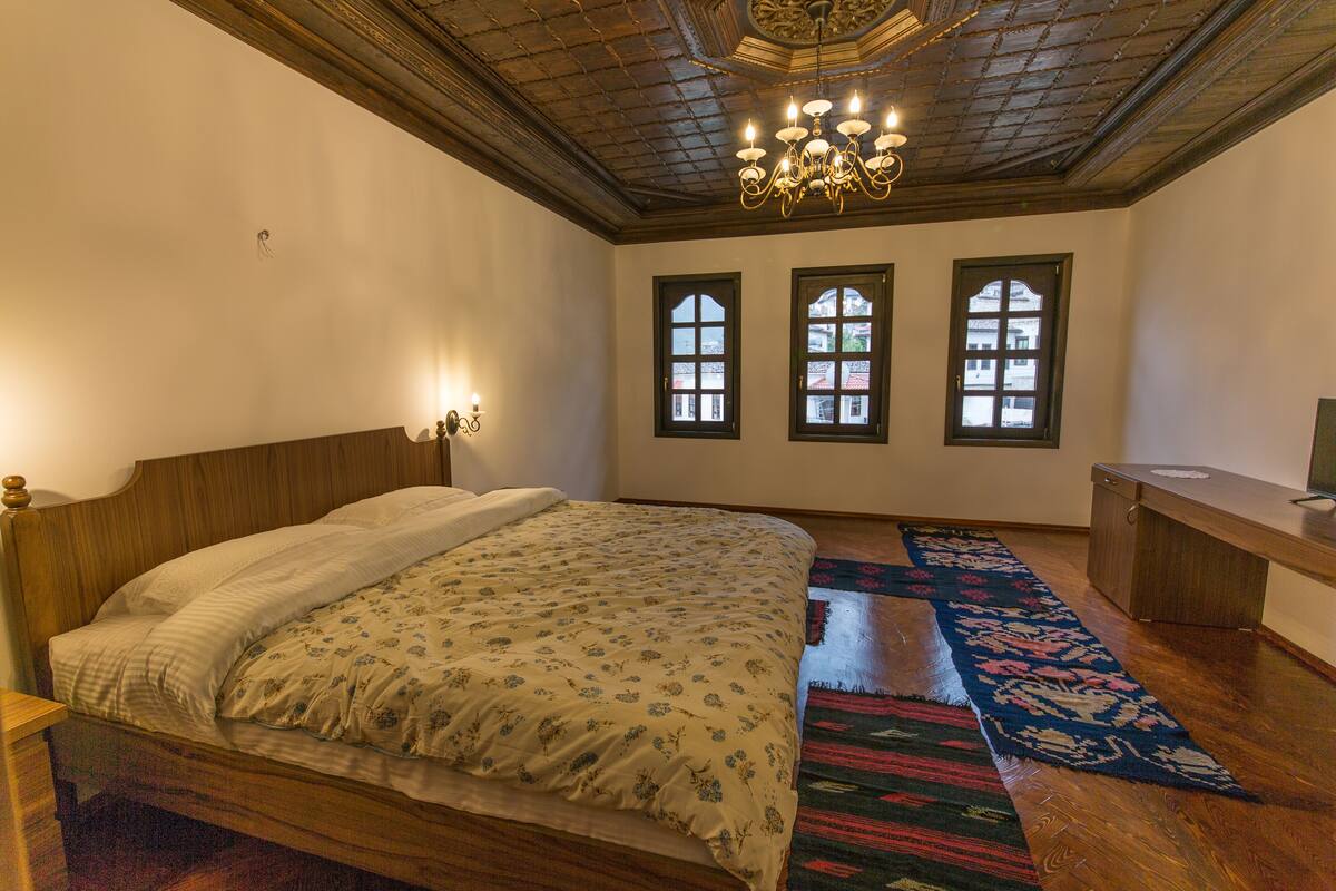A bedroom with a wooden bed, a chandelier, and two windows with shutters.