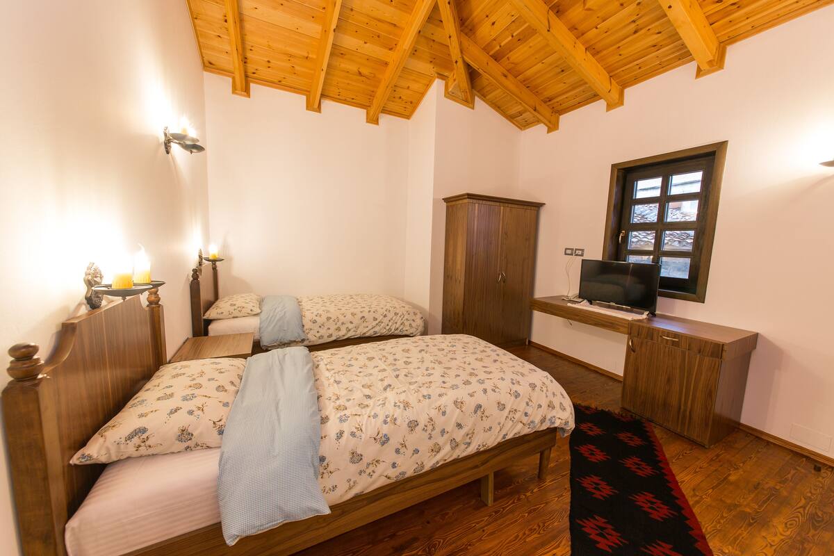 A bedroom with two wooden beds, a wooden wardrobe, a television, and a window.