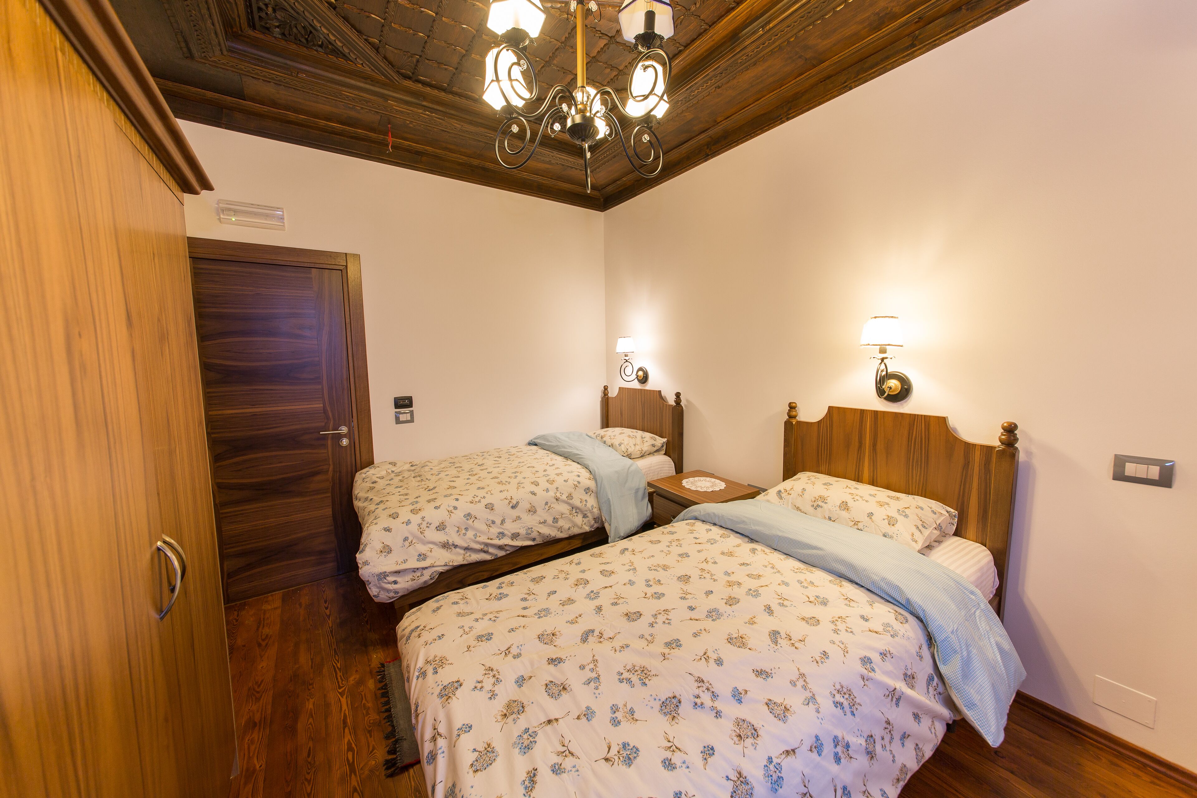 Une chambre avec deux lits en bois, une armoire en bois et un lustre.