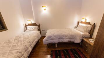 Un dormitorio pequeño y bien iluminado con dos camas individuales, cabeceros de madera, mesitas de noche y una mesilla con teléfono.