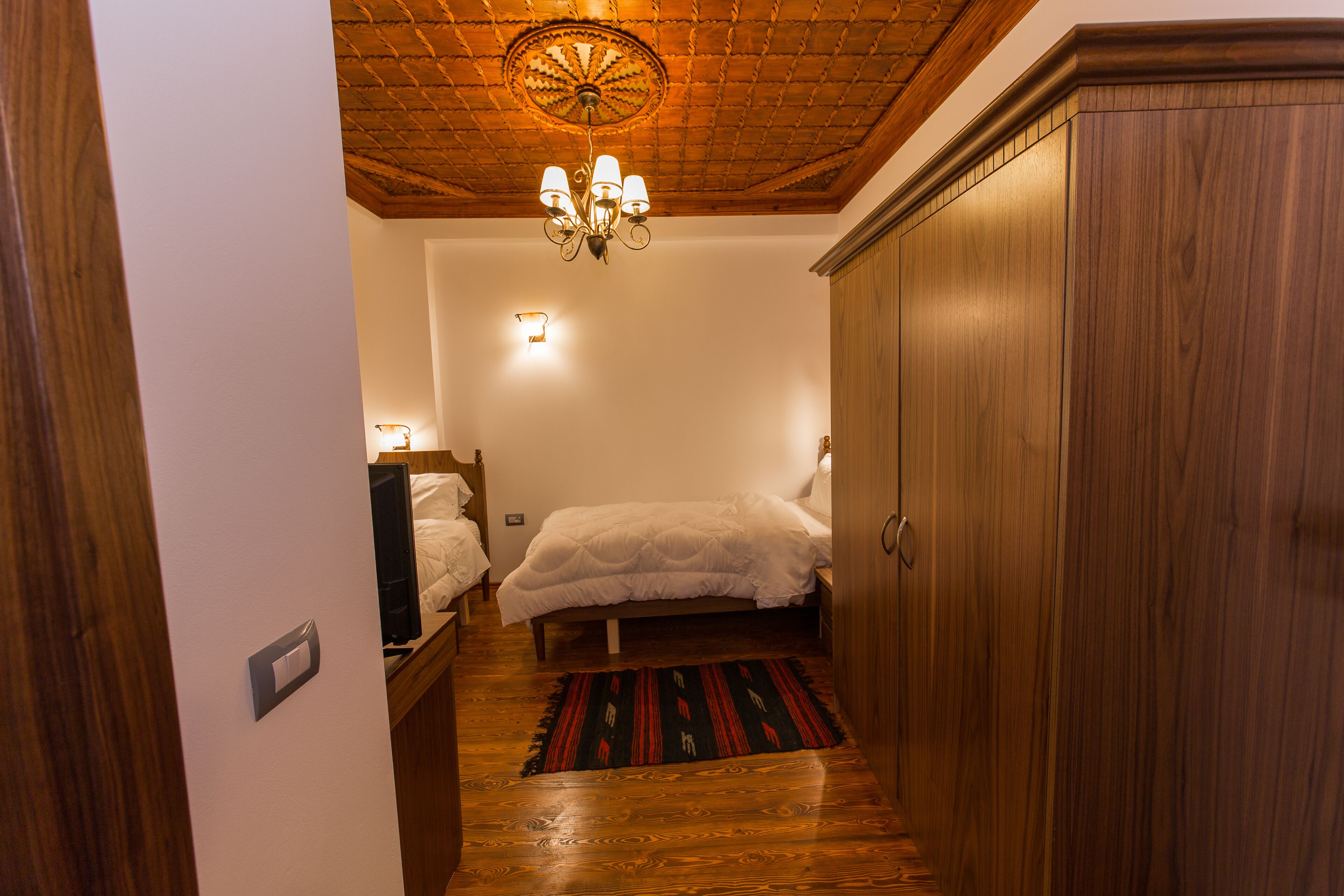 Ein Schlafzimmer mit Holzboden, einer Chandelüster, einem Bett mit weißer Bettwäsche, einem Nachttisch und einem Kleiderschrank.
