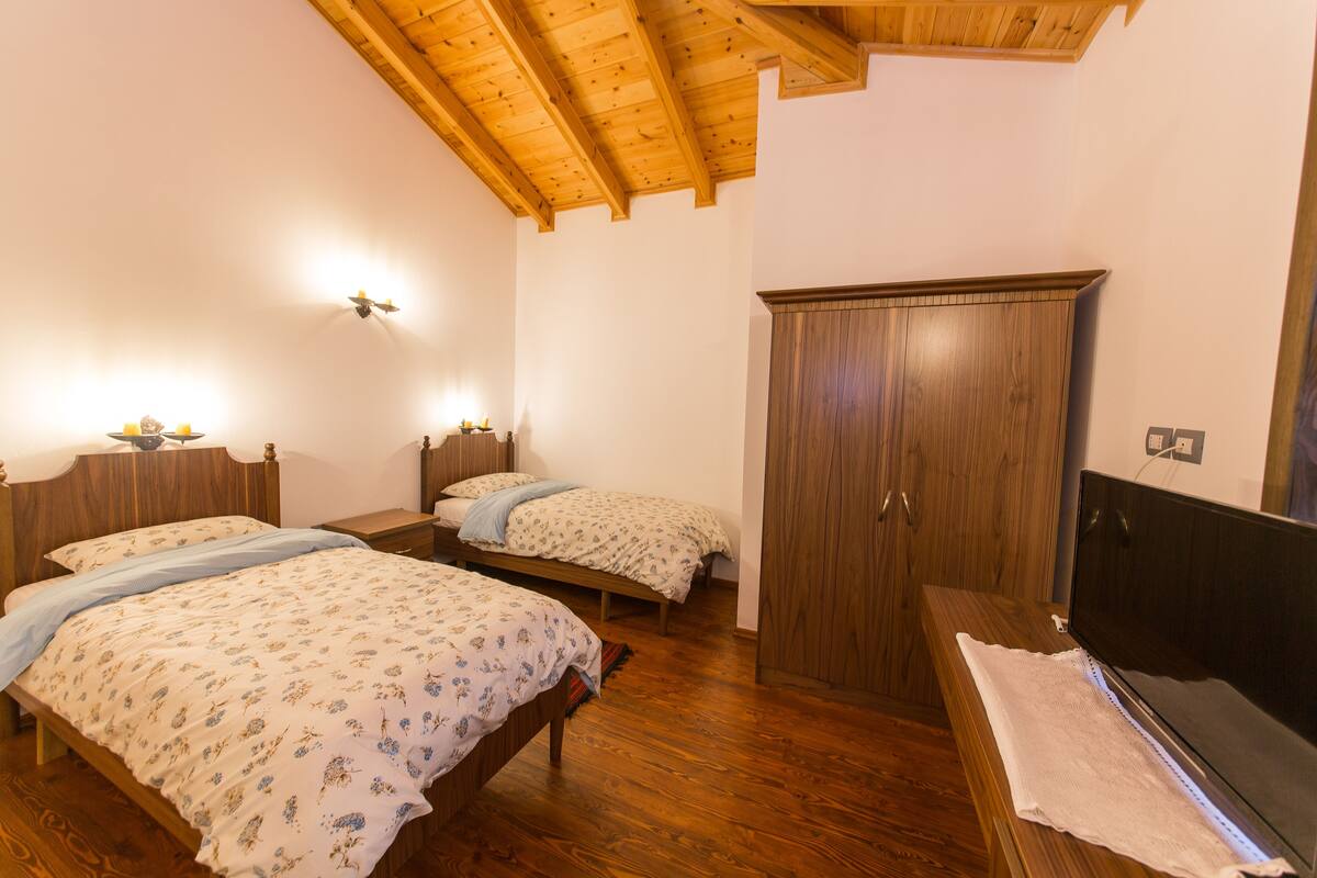 A bedroom with two beds, wooden flooring, a wardrobe, and a television.
