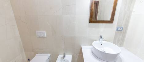 A modern bathroom with a toilet, bidet, and a sink with a mirror above it.