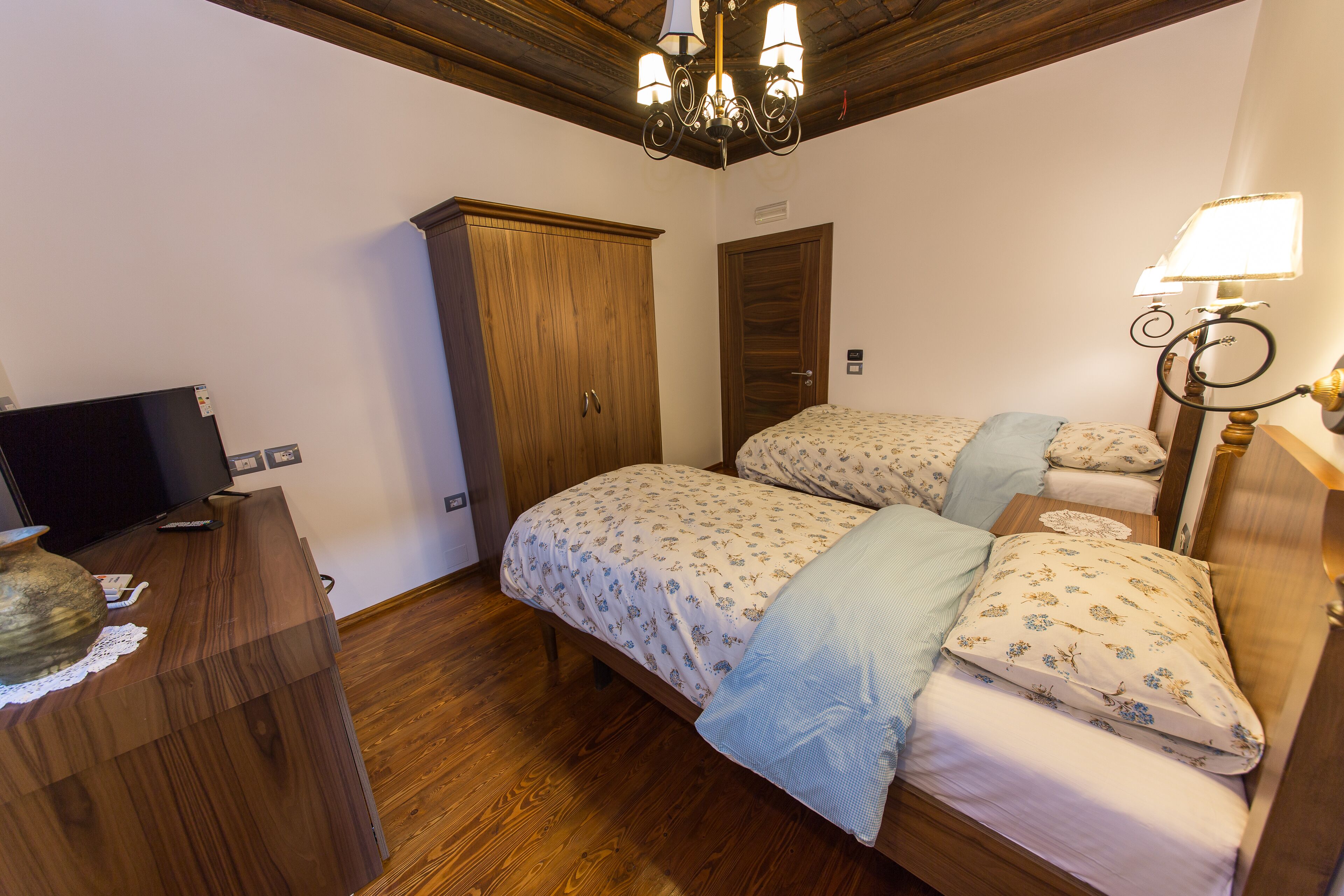 Une chambre avec deux lits, une armoire en bois, une télévision et un lustre.