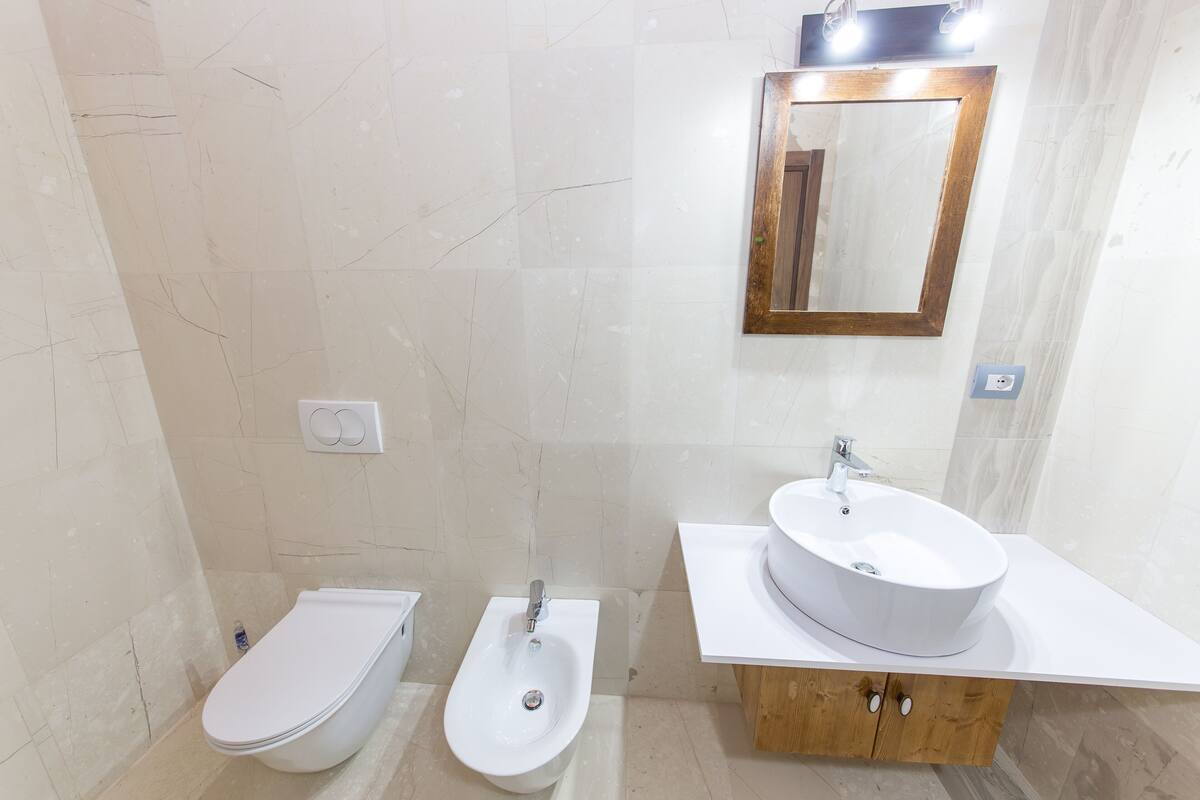 A modern bathroom with a toilet, bidet, and a sink with a mirror above.