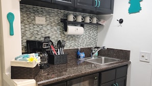 Uma cozinha compacta com armários escuros, bancada de granito e uma pia pequena.