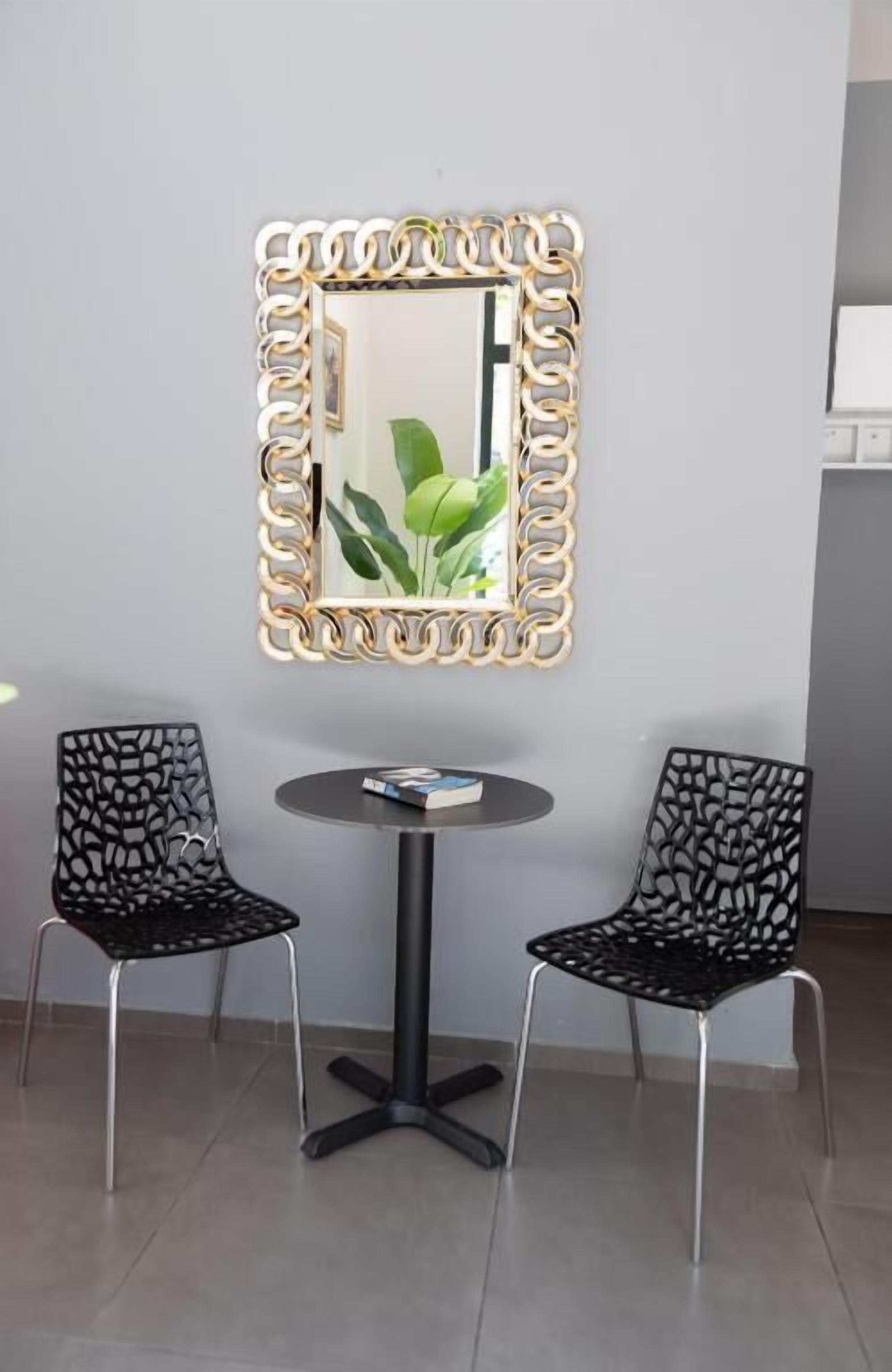 Quarto com uma mesa redonda e duas cadeiras, um espelho decorativo e uma planta.