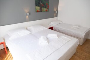 Habitación de hotel con dos camas, cada una con ropa de cama y almohadas blancas, y una mesita de noche roja.