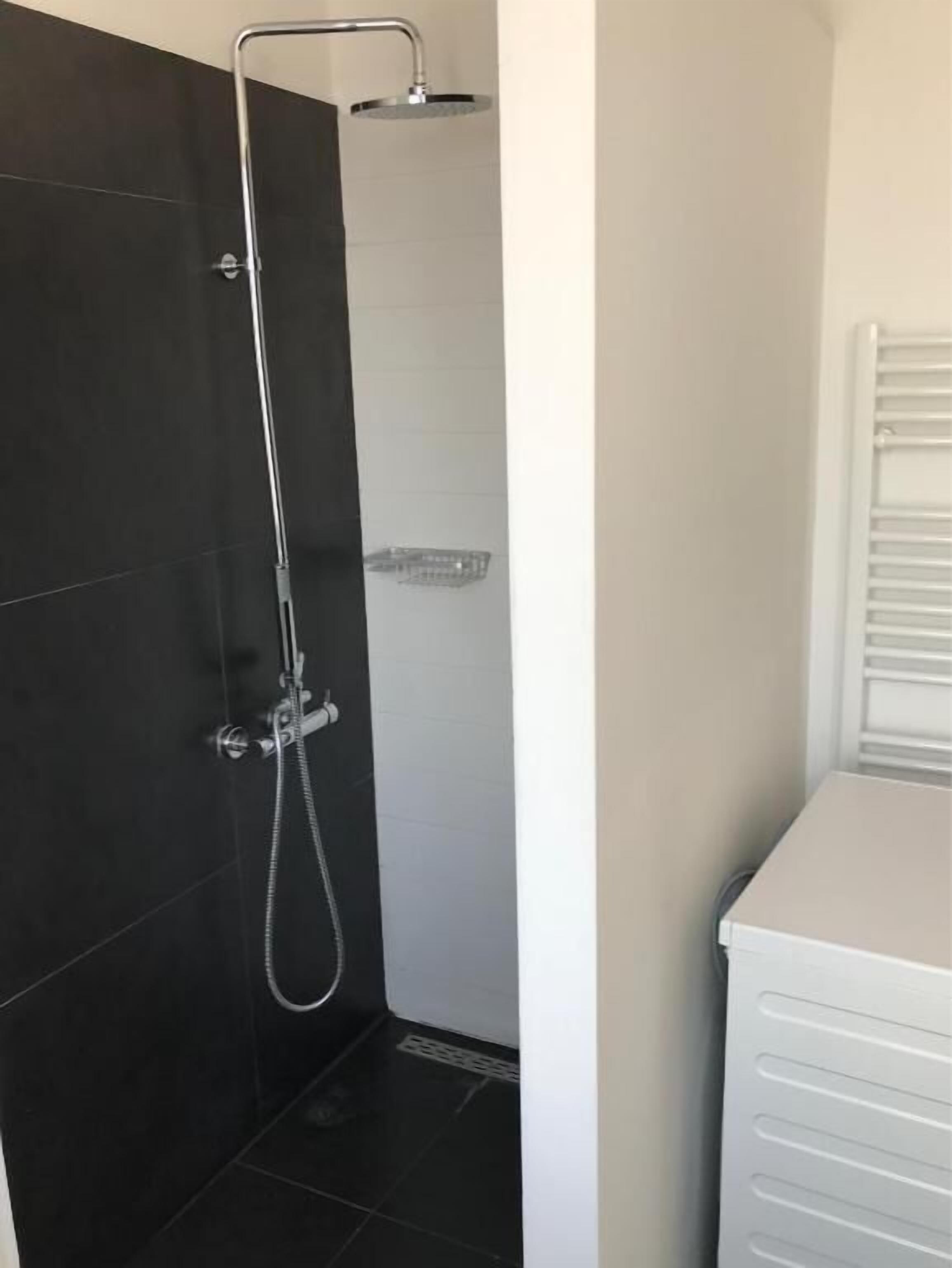 A shower with a handheld showerhead and a wall-mounted faucet.