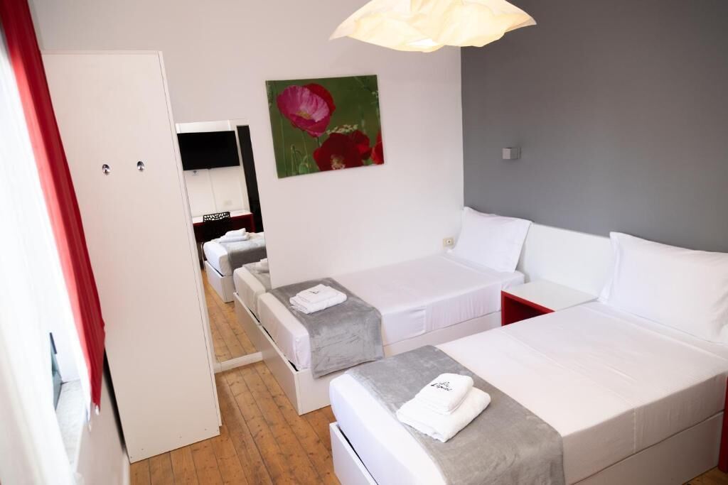 Habitació d'hotel amb dos llits, una cadira vermella, un armari blanc i un quadre a la paret.