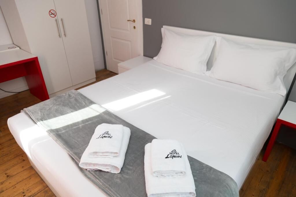 Ett hotellrum med en säng, två vita kuddar, ett grått täcke och två handdukar med hotellets logotyp.