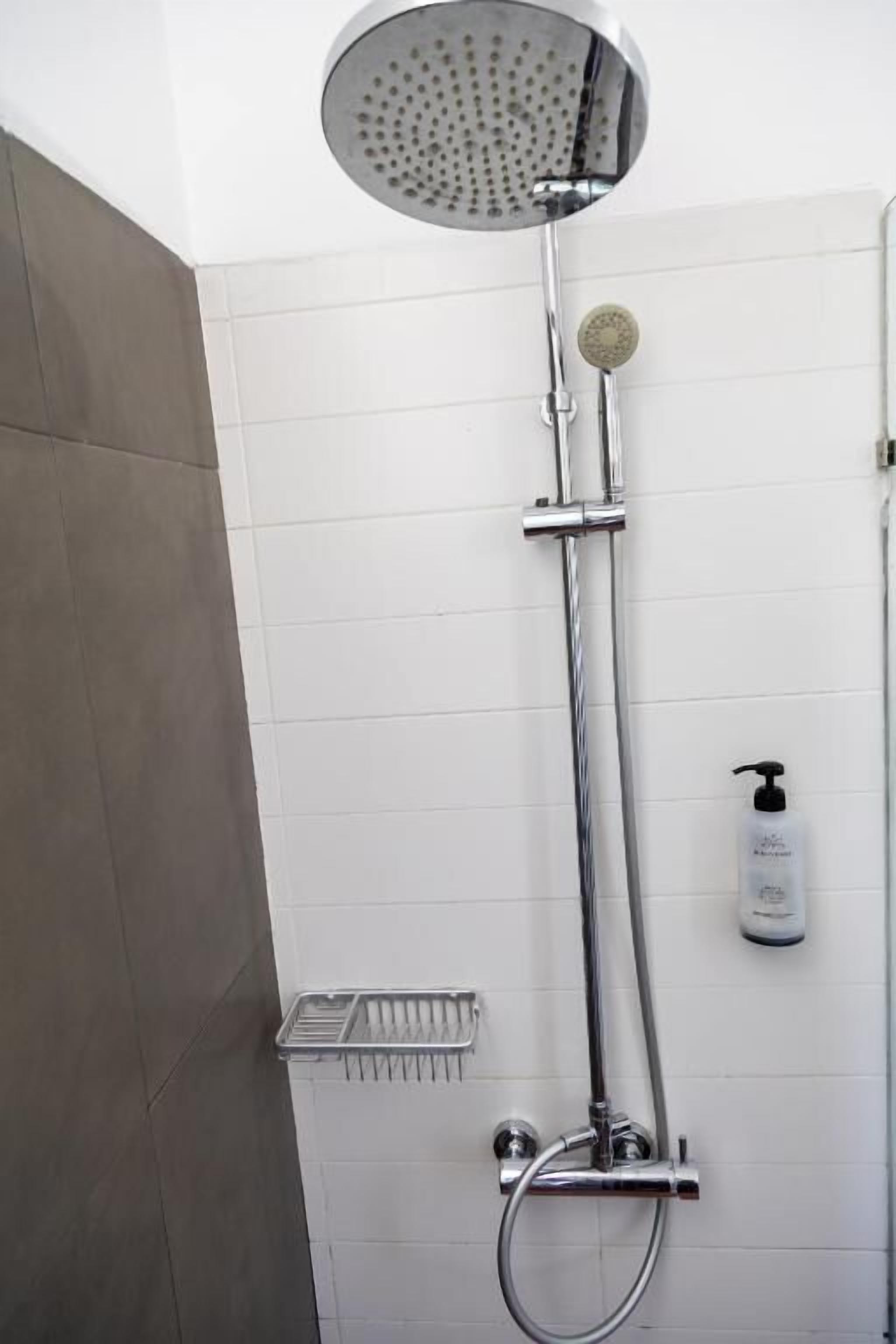 Une douche équipée d’un pommeau de douche rond, d’un pommeau de douche à main et d’un distributeur de savon fixé au mur.