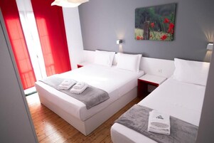 Una habitación de hotel moderna con una cama grande, una cama más pequeña y una pared de acento roja.