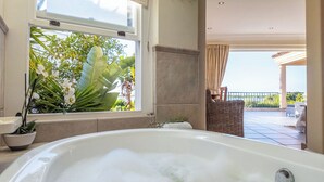 A bathroom with a bathtub, a window with plants, and a view of a balcony. - Luxury  Ocean View Villa, waterfront with pool -Plettenberg Bay (Plettenberg Bay)