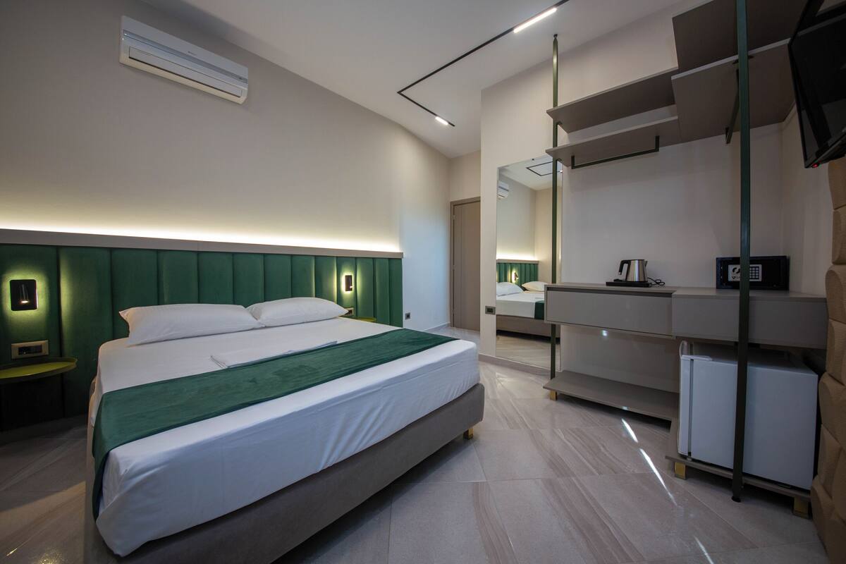 A modern hotel room with a large bed, bedside tables, a desk, and a mirror.