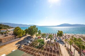 A beachside view with a pool area, umbrellas, and a clear view of the sea and mountains. - Hotel Royal (Orikum)