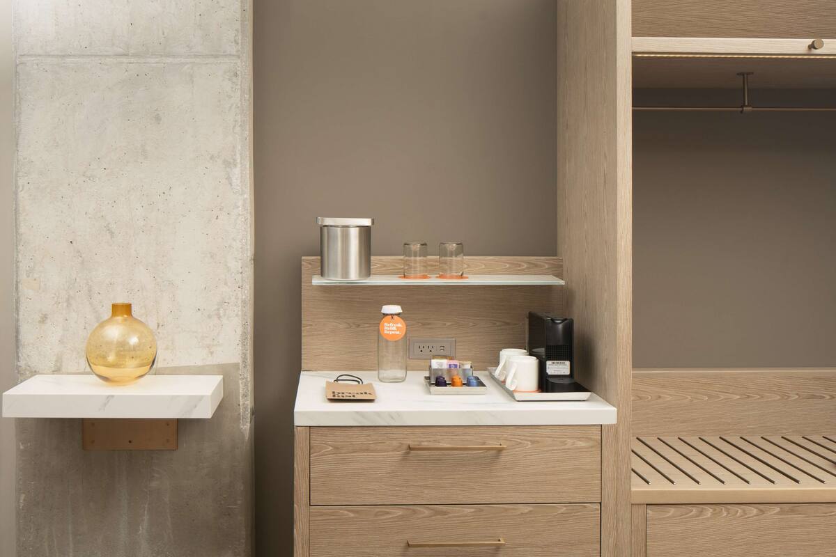 Ein Hotelzimmer mit einem Holzkonsolenmöbel, einer kleinen Ablage mit einer Vase, einer Kaffeemaschine und einer Wasserflasche.