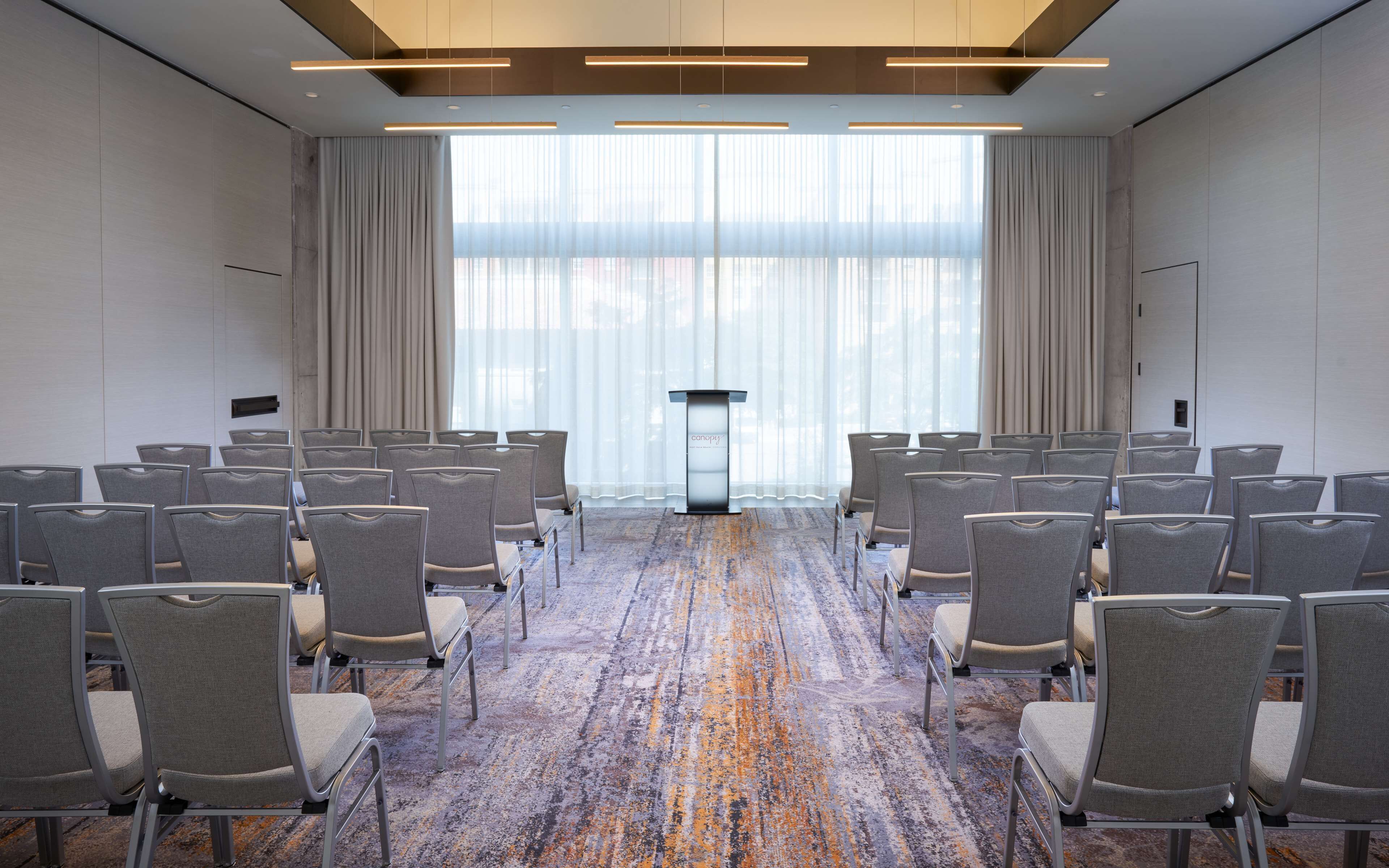 A conference room with rows of chairs, a podium, and large windows with curtains.