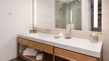 A modern bathroom with a large mirror, two sinks, a shower, and a wooden vanity with storage.