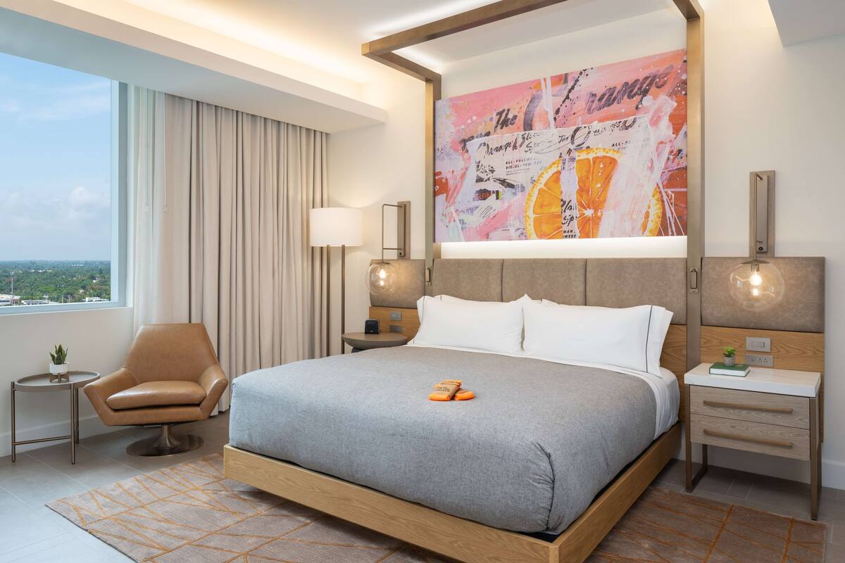 Ein modernes Hotelzimmer mit einem großen Bett, einem Sessel, einem Nachttisch und Blick auf die Stadt.
