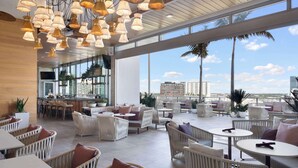 Ein großzügiger Außenbereich mit Lounge-Möbeln aus Rattan, runden Tischen und hängenden Pendelleuchten.