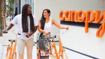 To personer på cykler foran en bygning med et stort orange skilt, hvor der står 'canopy'.