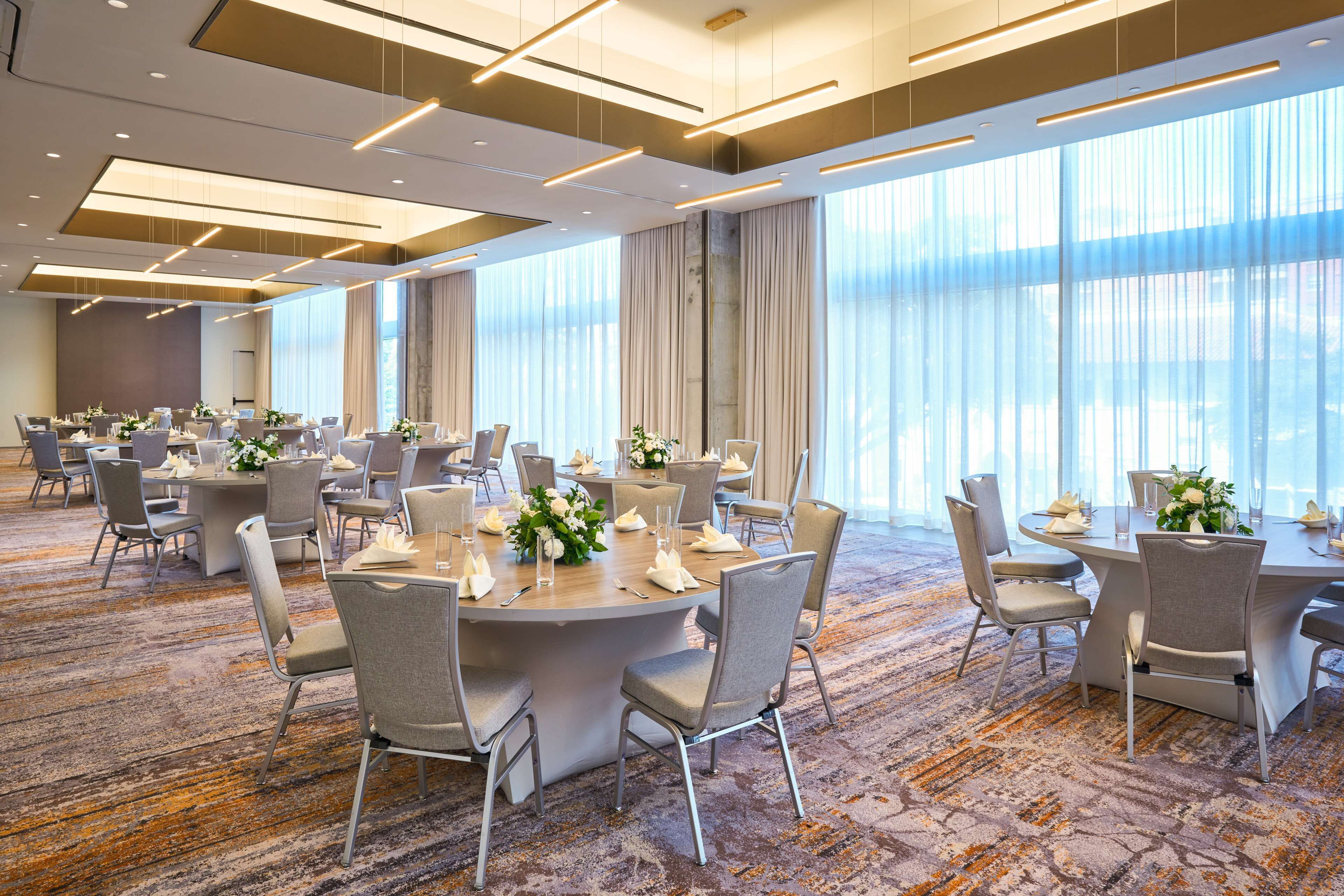 A spacious conference room with round tables, grey upholstered chairs, and a carpeted floor.