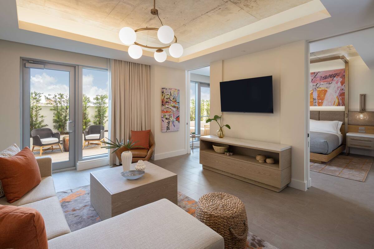 Ein modernes Wohnzimmer mit Sofa, Couchtisch und Fernseher. Ein Schiebetürfenster führt zu einem Außenbereich mit Sitzgelegenheiten.